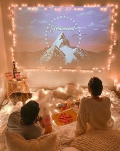 two people sitting on a bed with lights around them and a projection screen behind them