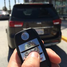 a person holding up a cell phone in front of a car on the street with other cars behind them