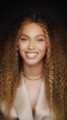 a woman with long blonde hair smiling at the camera, wearing a white shirt and gold necklace