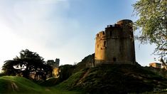 an old castle sitting on top of a lush green hillside under a blue cloudy sky