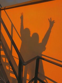 the shadow of a person on an orange wall with their hand up in the air