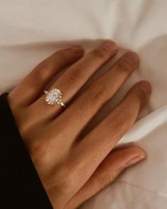 a woman's hand with a diamond ring on top of her left hand, resting against a white sheet