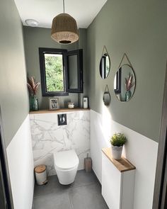 a white toilet sitting next to a window in a bathroom under a light fixture with three mirrors on the wall