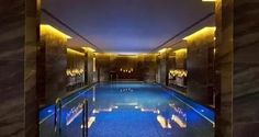 an indoor swimming pool surrounded by marble walls and flooring with lights on either side