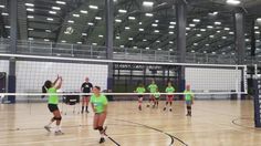 people playing volleyball in an indoor gym with lights on the ceiling and hard wood floor