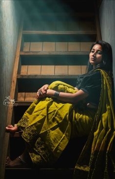 a woman in a yellow sari sitting on some stairs