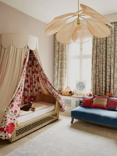 a canopy bed in a bedroom with floral curtains on the windowsill and a blue couch