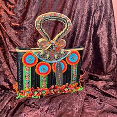 a handbag decorated with beads and feathers on a velvet background, in front of a red backdrop