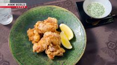 a green plate topped with fried chicken next to a bowl of sauce and lemon wedges