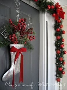 a christmas stocking hanging on the front door next to a wreath with red berries and greenery