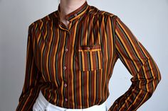 Vintage striped pattern blouse in burnt orange, brick red, black and tobacco green stripes in different sizes, a high neck collar and a single small chest pocket. Made in Switzerland Era - 70s / early 80s Material - 100% polyester Size - marked 42, fits like contemporary M, shown on size 38 EU/ 8 US, cup size A Please look at measurements below to see if the blouse will fit you: Approximate. Measurements ( taken when blouse lying flat, double armpit to armpit ): Shoulder to Shoulder (from seam t 80s Secretary, Orange Brick, High Neck Collar, Pattern Blouse, Brick Red, Small Chest, Blouse Patterns, Striped Blouse, Neck Collar