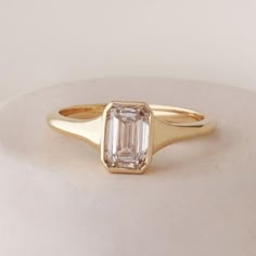 a gold ring with an emerald cut diamond in the center, on a white surface