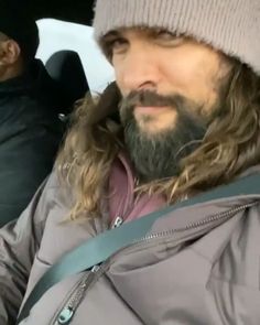 a man with long hair and beard wearing a beanie sitting in the back seat of a car