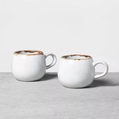 two white coffee mugs with brown rims sitting side by side on a gray surface