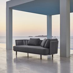 a couch sitting on top of a cement floor next to the ocean