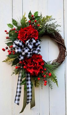 a wreath with red flowers and greenery hanging on a white wall