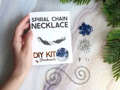 a hand holding a book about chain necklaces on top of a table next to plants