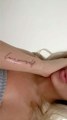 a woman's arm with the word love yourself tattooed on her left arm and behind her head