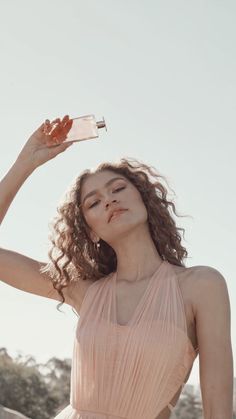 a woman in a pink dress is holding a bottle and looking up at the sky