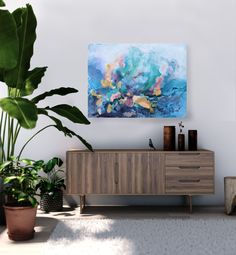 a painting is hanging on the wall next to a wooden cabinet and potted plant