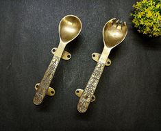 two spoons and a fork are sitting on a table next to a potted plant