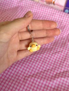 a hand holding a small yellow bear keychain on a pink and white checkered table cloth