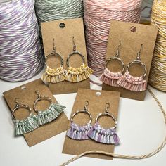 four pairs of earrings with tassels on them sitting in front of yarn spools