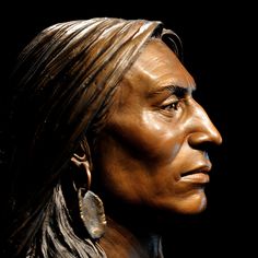 a statue of a native american man with long hair and earrings on his head, looking to the side