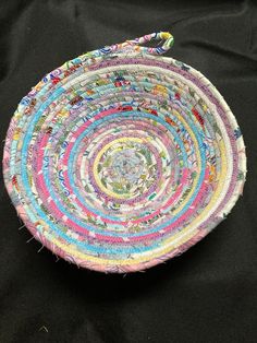 a multicolored woven bowl sitting on top of a black cloth