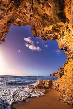 the sun is shining through an opening in a rock formation at the beach with waves crashing on the shore