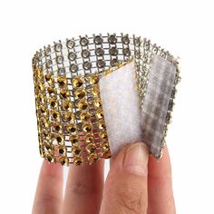 a hand holding two pieces of fabric and some gold beads on top of each other