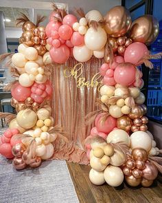 a table topped with lots of balloons on top of a wooden table covered in pink and gold