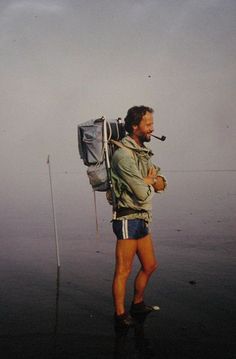 a man with a backpack and a pipe in his mouth is standing on the beach