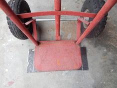 a red cart sitting on top of a cement floor next to a metal pole and tire