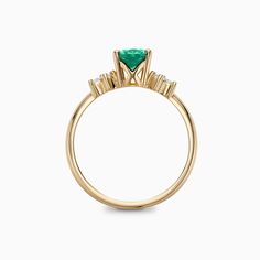 a yellow gold ring with an emerald stone and three diamonds on the band, set in 18k yellow gold