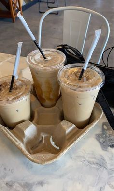 three iced coffees are sitting on a tray with two straws in each cup