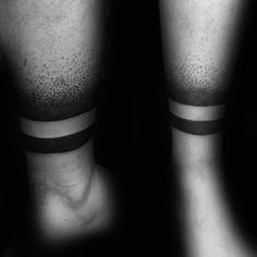 black and white photograph of two legs with tattoos on them, one has a band around the leg