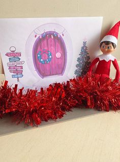 an elf is standing next to a card with a red tinsel garland on it