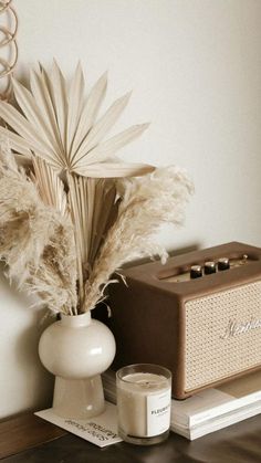 a white vase with some dried plants in it and a radio on the table next to it