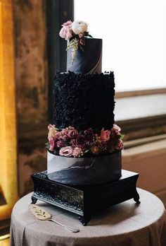 a three tiered black wedding cake with flowers on top