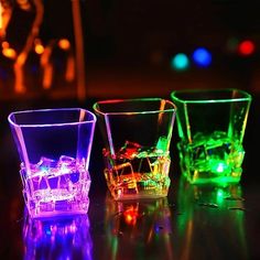 three different colored glasses sitting next to each other on top of a black table with colorful lights in the background