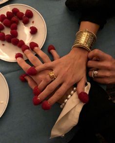 two people holding hands with red raspberries on plates in the foreground, and one person wearing gold bracelets