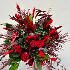 a vase filled with red flowers and greenery next to a white wall in the background