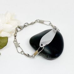 a white flower sitting on top of a black rock next to a silver chain bracelet