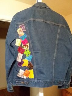 a jean jacket with colorful patches on it hanging from a closet door in a home