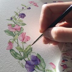 a person is drawing flowers on a piece of paper with watercolors and ink