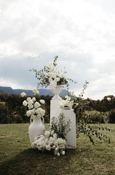 two white vases with flowers and greenery on the grass