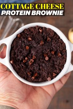 a hand holding a white bowl filled with chocolate cheese protein brownie