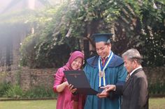 two men and a woman in graduation gowns are looking at a piece of paper