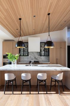 a kitchen with wooden ceiling and white counter tops, three chairs in front of the island